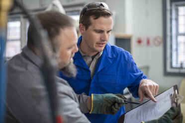 Männliche Automechaniker, die auf ein Klemmbrett in einer Reparaturwerkstatt zeigen - ISF02959