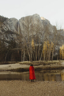 Rückansicht einer in eine rote Decke eingewickelten Frau mit Blick auf einen Berg, Yosemite National Park, Kalifornien, USA - ISF02965