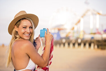 Porträt einer jungen Frau im Bikinioberteil, die einen Vergnügungspark am Strand fotografiert, Santa Monica, Kalifornien, USA - ISF03041