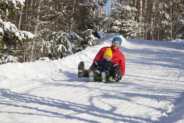 Man and son tobogganing in snow covered forest - ISF03086