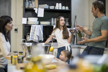 Husband and wife talking to daughter in kitchen, toddler girl reaching for lemons - ISF03105