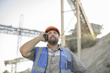 Quarry worker in quarry, using smartphone, looking up - ISF03186