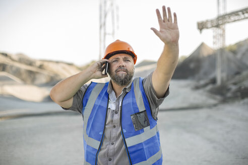 Steinbrucharbeiter in einem Steinbruch, der ein Smartphone benutzt und mit der Hand gestikuliert - ISF03187