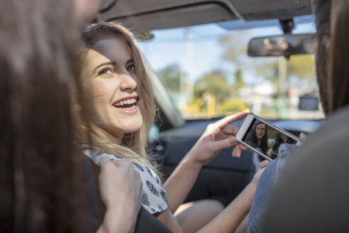 Drei Frauen im Auto, die auf ihr Smartphone schauen - ISF03203
