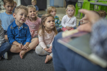 Kleine Kinder sitzen auf einem Teppich im Klassenzimmer und hören dem Lehrer vor der Klasse zu - ISF03218