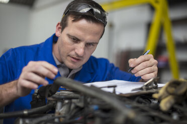 Männlicher Automechaniker mit Klemmbrett, der einen Automotor in einer Werkstatt überprüft - ISF03226