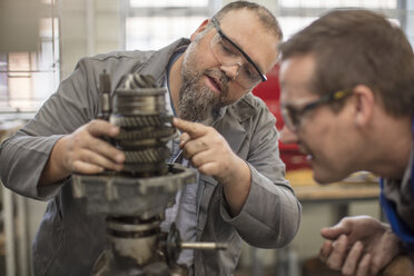 Male car mechanics pointing at car part in repair garage - ISF03231