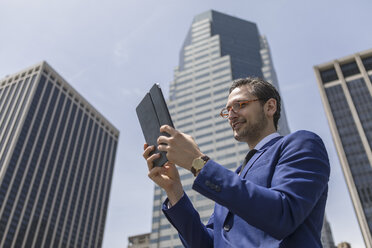 Lächelnder junger Geschäftsmann mit Blick auf ein digitales Tablet vor New Yorker Wolkenkratzern, USA - ISF03253