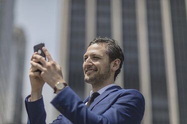 Lächelnder junger Geschäftsmann macht ein Selfie vor einem Bürogebäude, New York, USA - ISF03254