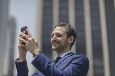 Smiling young businessman taking selfie outside office building, New York, USA - ISF03254