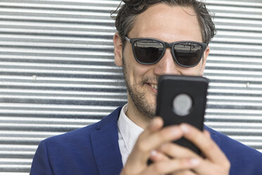 Junger Geschäftsmann mit Sonnenbrille schaut auf sein Smartphone - ISF03257