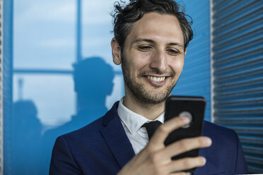 Smiling young businessman in city looking at smartphone - ISF03259