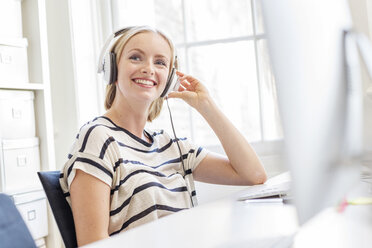 Female designer listening to headphones at creative studio desk - ISF03371