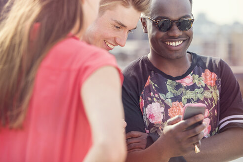 Drei junge erwachsene Freunde schauen bei einer Dachparty in London, UK, auf ihr Smartphone - ISF03422