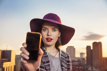 Porträt einer jungen Frau, die ein Smartphone-Selfie bei Sonnenuntergang auf einer Dachparty in London, Vereinigtes Königreich, macht - ISF03434