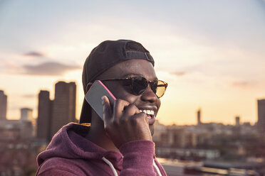 Junger Mann telefoniert mit seinem Smartphone bei Sonnenuntergang auf einer Dachparty in London, Großbritannien - ISF03436