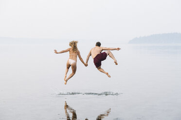 Junges Paar am Strand, Hände haltend, springend, in der Luft, Rückansicht - ISF03542