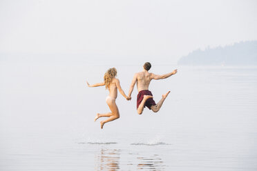 Young couple on beach, holding hands, jumping, mid air, rear view - ISF03543