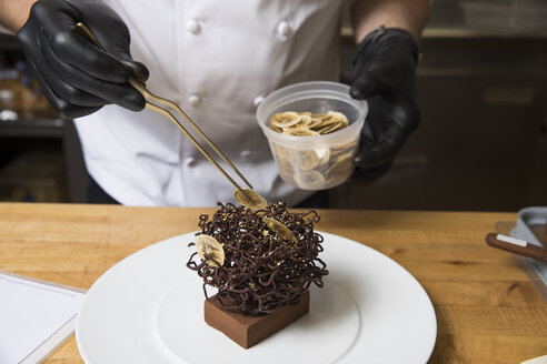 Chef placing slices of dried banana on chocolate nest cake decoration - ISF03563