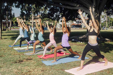 Schoolgirls practicing yoga warrior one pose on school sports field - ISF03566