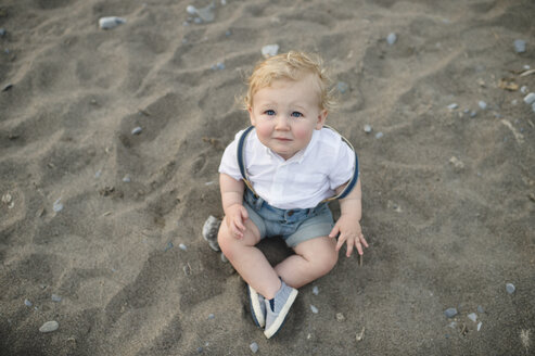 Overhead-Porträt eines männlichen Kleinkindes, das auf Sand sitzt - ISF03624