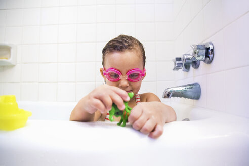 Girl wearing swimming goggles playing with toys in bath - ISF03653