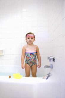 Portrait of girl wearing swimming goggles standing in bath - ISF03655