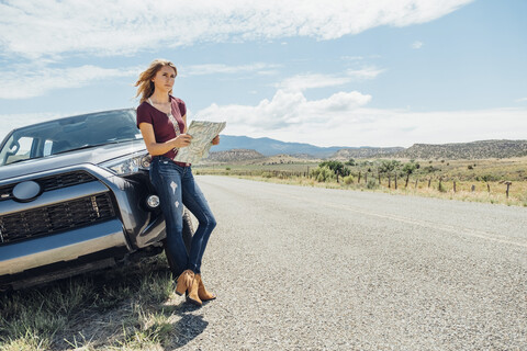 Frau mit Karte an Auto gelehnt, lizenzfreies Stockfoto