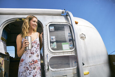 Young woman with coffee looking out from airstream doorway - ISF03677