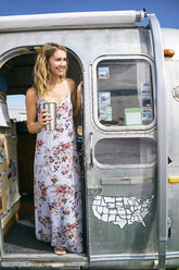 Young woman wearing maxi dress looking out from airstream doorway - ISF03678
