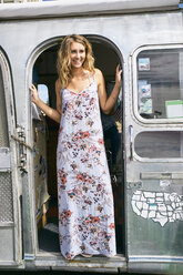 Young woman in maxi dress looking out from airstream doorway - ISF03679