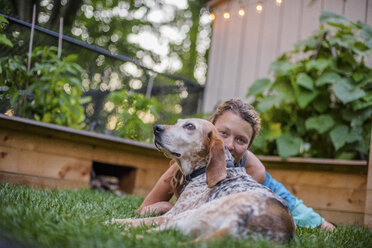 Porträt einer reifen Frau und eines Hundes, die zusammen auf dem Gartenrasen liegen - ISF03682