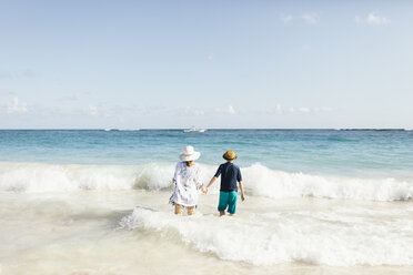 Mother and son, holding hands, standing in surf on beach, rear view - ISF03691