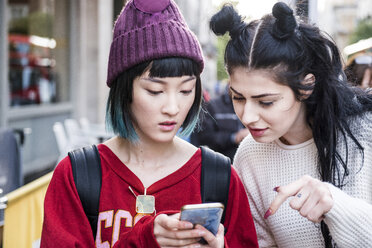 Zwei junge stilvolle Frauen schauen auf Smartphone auf der Straße der Stadt - ISF03721