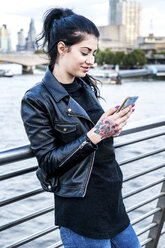 Junge Frau schaut auf der Millennium-Fußgängerbrücke auf ihr Smartphone, London, UK - ISF03727