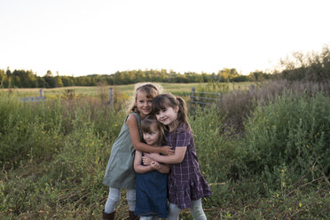 Portrait of three young girls standing together in field, hugging - ISF03771