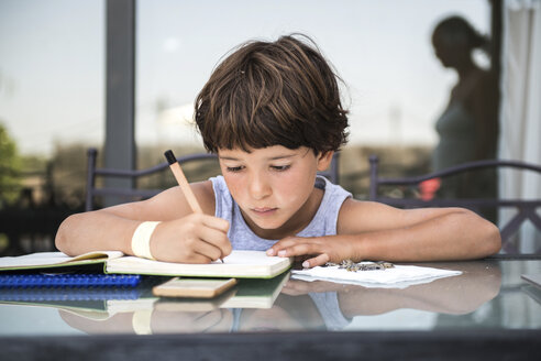 Boy at table writing in workbook - ISF03790