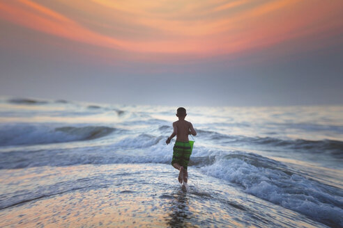 Junge läuft bei Sonnenuntergang ins Meer, North Myrtle Beach, South Carolina, Vereinigte Staaten - ISF03791