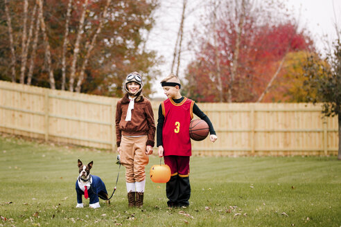 Porträt eines Jungen, einer Zwillingsschwester und eines Boston Terriers in Halloween-Kostümen im Garten - ISF03817