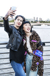 Two young stylish women taking smartphone selfie on millennium footbridge, London, UK - ISF03825