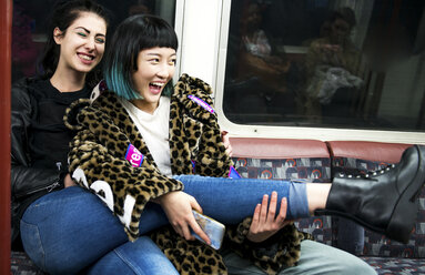 Two young stylish women laughing on underground train carriage - ISF03827