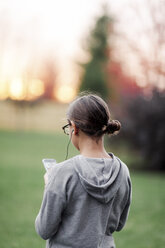 Rear view of girl listening to earphone music looking at smartphone in garden - ISF03864