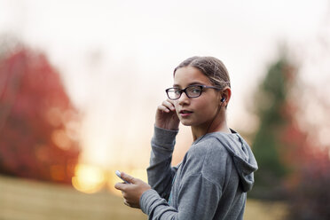 Porträt eines Mädchens, das mit seinem Smartphone Musik hört und über die Schulter im Garten schaut - ISF03865