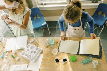 Overhead view of two girls doing science experiment, reading chemistry set instructions - ISF03871