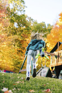 Rückansicht eines Mädchens, das mit einer Spielzeugrakete im Garten läuft - ISF03891