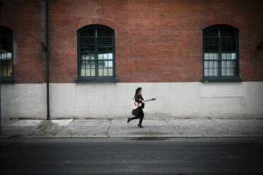 Junge Frau läuft mit Akustikgitarre auf dem Bürgersteig der Stadt - ISF03900
