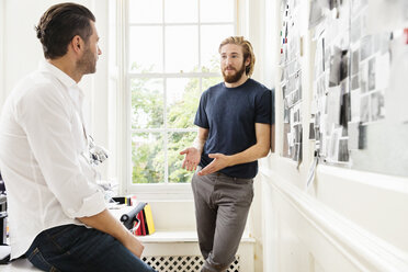 Young male designer explaining mood board idea to colleague in creative studio - ISF03909
