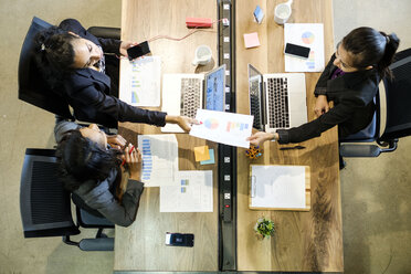 Drei Geschäftsfrauen sitzen am Schreibtisch, benutzen Laptops, halten ein Smartphone, reichen ein Dokument weiter, Draufsicht - ISF03975