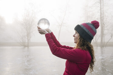 Frau hält Kristallkugel auf zugefrorenem See hoch - ISF03982