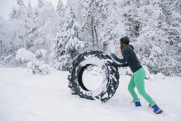 Frau rollt Reifen durch Schnee - ISF04005